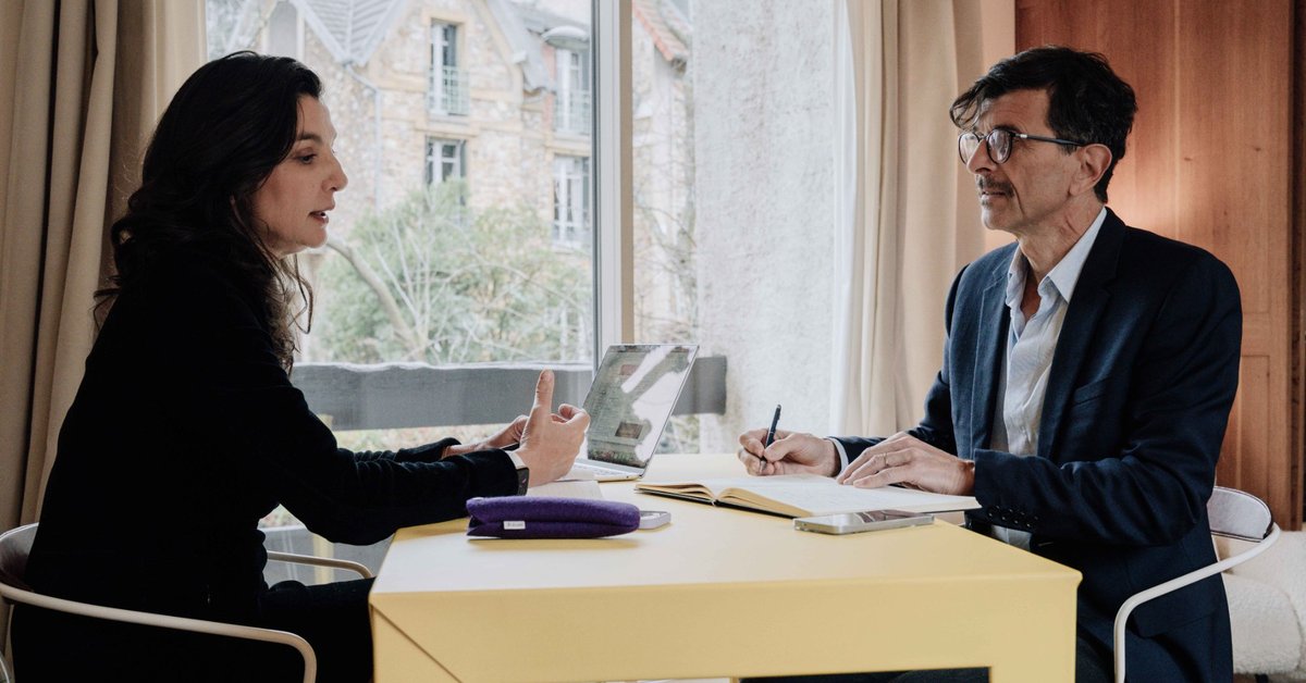 Caroline de la Mardière, agente de conférenciers, en échange de travail autour d'une table avec un interlocuteur qui prend des notes